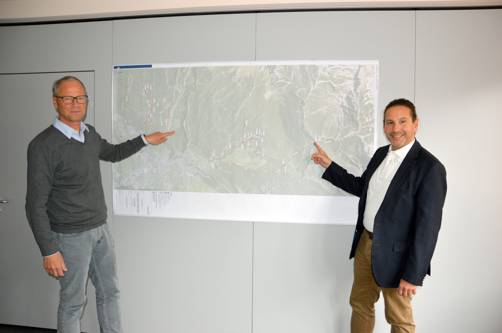 Zwei Männer zeigen auf eine Karte an der Wand.